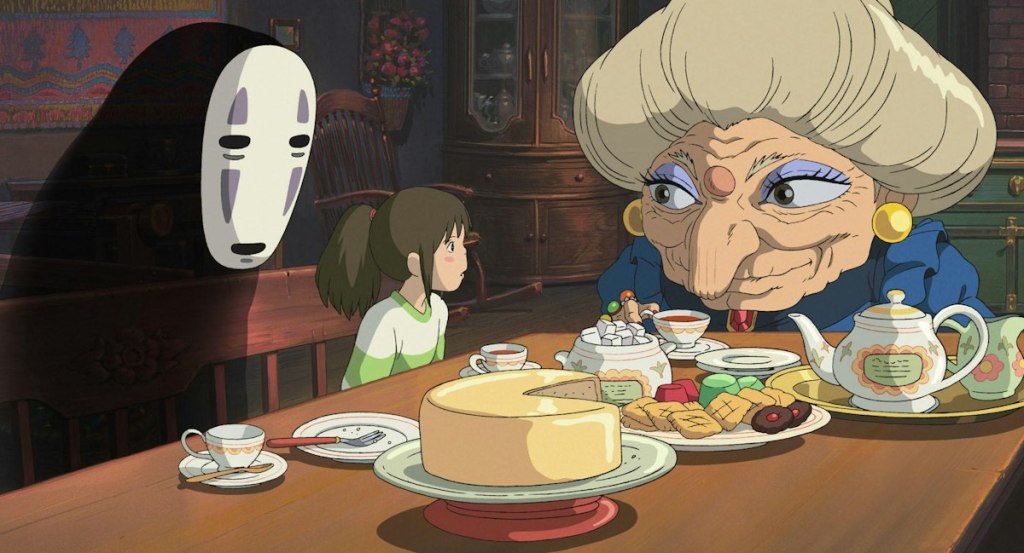 Chihiro and No-Face sit with Zeniba at a table filled with tea and food in Spirited Away