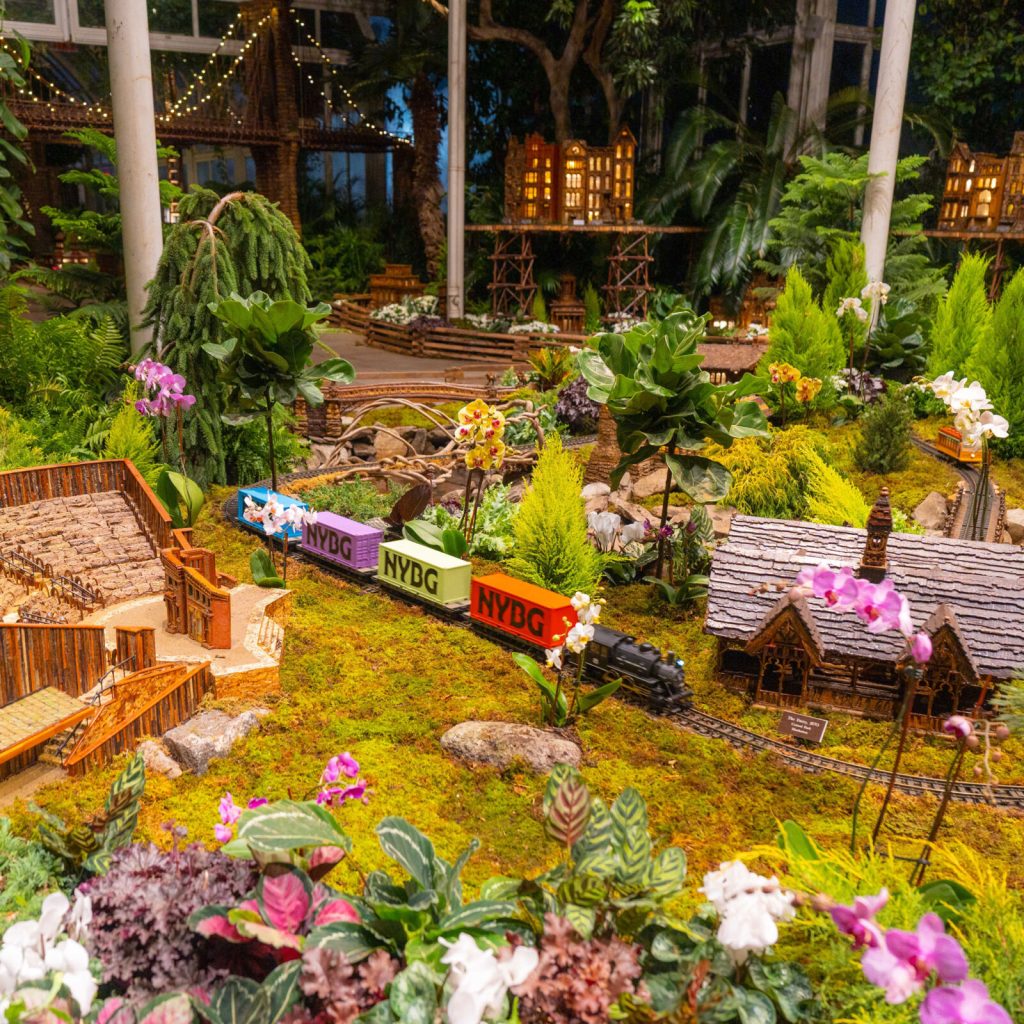 Miniature NYBG train winding past model buildings and plants in the Holiday Train Show