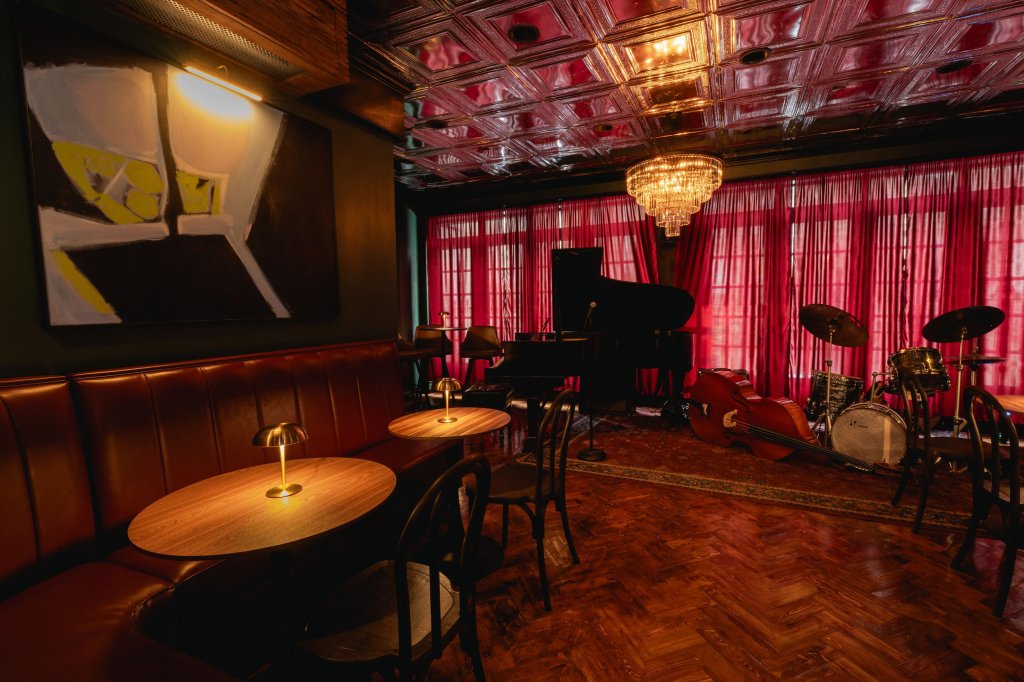 Intimate music room at One Flight Up, with a piano, double bass, drum kit and red curtains
